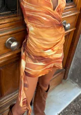 Vestido corto con estampado abstracto en tonos naranja, blanco y marrón. Diseño con escote halter y espalda descubierta.