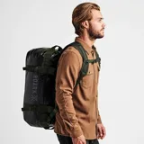 Bolso de viaje tipo duffle negro con detalles en verde, marca Roark, modelo Pony Keg 60L. Tiene doble asa de mano con agarre acolchado, correa de hombro ajustable y extraíble, bolsillo frontal con cierre y logo estampado. Se puede usar como bolso de mano o como mochila.