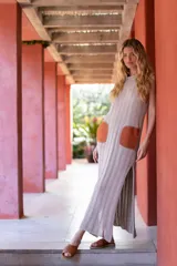 Vestido largo tejido en hilo de algodón color gris claro, con corte recto, tajos laterales y bolsillos de cuero color marrón.