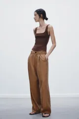 Pantalón de vestir color marrón claro, de tiro medio, corte ancho y con pliegues frontales.
