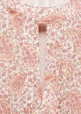 Vestido corto con estampado paisley en tonos rosa y naranja, con escote redondo con abertura en forma de gota, mangas largas abullonadas con lazos en los puños y aberturas laterales en la cintura.