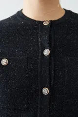 Chaqueta tejida negra con cuello redondo, cierre frontal con botones dorados, bolsillos delanteros y corte clásico.