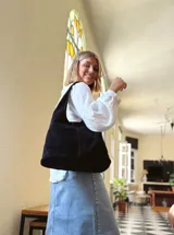 Bolso tipo tote bag negro de cuero, con costuras a la vista y manijas cortas.