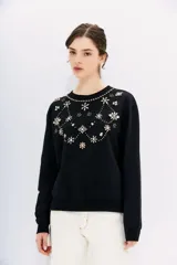 Buzo negro de algodón con cuello redondo y mangas largas. Presenta apliques bordados de piedras con forma de flores y círculos en el frente.