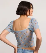Blusa cropped de tule celeste con estampado floral, escote corazón, mangas cortas sueltas con acabado frufru y fruncido en el busto.