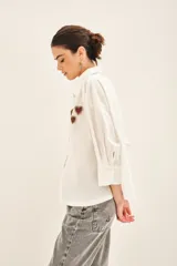 Camisa blanca de algodón con bordados de corazones rojos y dorados en el delantero. Tiene cartera en el delantero y fruncido en el centro de la espalda.