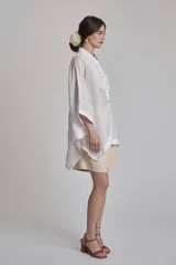 Camisa blanca de lino con cuello clásico, cierre frontal con botones y mangas anchas 3/4. Presenta detalles de bordado calado en el frente y puños.