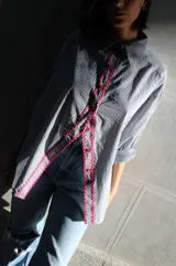 Camisa de poplin negro rayado con corte cómodo, mangas 3/4 y detalles ondeados al frente con zigzag de algodón fucsia y botones fucsia.