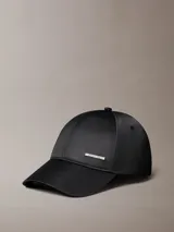 Gorra de béisbol negra con acabado satinado y visera curva. Presenta una placa metálica rectangular con el logo de Calvin Klein grabado en la parte frontal.