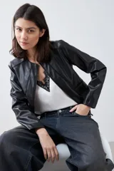 Chaqueta corta de cuero sintético color negro, con cuello redondo y cierre frontal. Presenta detalle de pasamanería en hombros y cuello.