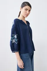 Blusa blanca de estilo boho con bordados de flores en amarillo y azul en mangas y escote.