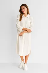 Vestido camisero blanco de lino, corte holgado, largo midi, con cuello camisero, abotonadura frontal y mangas 3/4 con puños. Incluye un bolsillo de parche en el pecho y aberturas laterales en el ruedo.
