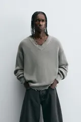 Sweater gris de punto con cuello en V, manga larga y terminaciones irregulares con efecto desgastado.