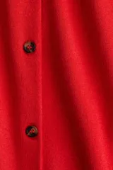 Cárdigan rojo de punto fino con cuello redondo, manga corta y cierre frontal con botones marrones. Tiene terminaciones acanaladas en cuello, puños y bajo.