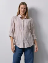 Camisa color beige con rayas verticales blancas, de lino, con cuello con solapa y abertura central con botones. Tiene un bolsillo aplicado en el pecho y mangas largas regulables con presilla y botón.