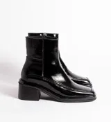 Bota corta de cuero charol negro, con caña baja, cierre lateral y taco cuadrado de madera.