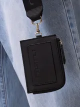 Billetera tarjetero negra de poliuretano con cierre y correa para colgar al cuello con logo Rusty estampado.