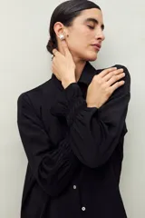 Camisa negra de manga larga con cuello clásico y botones frontales. El tejido presenta una textura arrugada o plisada, y los puños tienen un detalle fruncido o elástico.