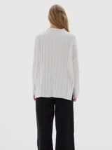 Buzo tejido color blanco, con cuello subido tipo polera, diseño oversized y largo con pequeños cortes laterales.