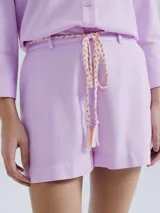 Short de lino blanco, de corte recto y tiro alto, con trabillas para cinturón y un lazo trenzado de color crudo anudado en el frente.