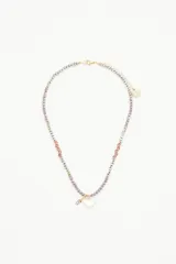 Collar corto de cuentas plateadas, lilas y marrones con dije transparente en forma de corazón.