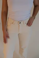 Jean mom color crema, de corte recto y tiro medio. Presenta dos bolsillos redondeados en la parte delantera y dos bolsillos en la parte trasera. Cierre con botón metálico y cremallera.