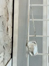 Bandolera plateada pequeña con diseño capitoneado, correa regulable con diseño combinado entre cintas de algodón, cuero y aritos metálicos.