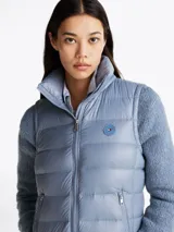 Chaleco acolchado celeste con cuello alto, cierre frontal con cremallera, dos bolsillos laterales con cremallera y logo de la marca en el pecho. Tiene mangas de tejido de punto. Repele el agua y tiene relleno de plumón.
