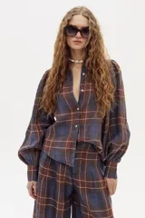 Camisa de lino a cuadros azules y marrones, con cuello camisero clásico, mangas largas abullonadas con puños ajustados con terminación de onditas, botones de nácar frontales y ruedo curvo, un poco más largo atrás.