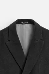 Abrigo corto de hombre color gris oscuro, con cuello con solapas de pico, manga larga acabada en puño con botón, bolsillos de solapa en cadera, detalle de bolsillo interior y bajo con abertura en centro espalda. Cierre frontal de botonadura.