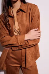 Camisa color marrón de gamuza sintética, con cuello clásico, cierre frontal con botones y mangas largas con puños abotonados.