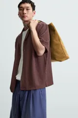 Camisa de manga corta con cuello bowling y calce relajado. Presenta un tejido con textura estructurada y efecto lavado, con cierre frontal de botones al tono.