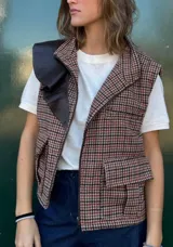 Chaleco con cierre frontal, cuello con solapa de cuero sintético, estampado a cuadros en tonos marrón, negro y rojo, y bolsillos delanteros con solapa.