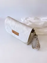 Bandolera color crudo con solapa de gamuza y cuerpo de cuero sintético texturizado. Tiene correa corta de cuero con tientos y forro de tela con bolsillo interno.