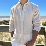 Camisa de manga larga color beige claro, con textura de lino arrugado y corte boxy. Presenta cuello camisero y cierre frontal de botones.