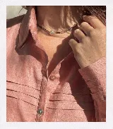 Camisa rosa de lino con tablitas simétricas en el frente, cuello recto y puños simples.