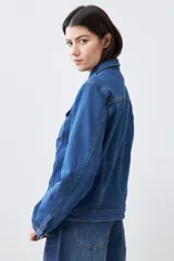 Campera clásica de jean color azul medio, con cuello clásico, cierre frontal con botones, bolsillos con solapa en el pecho y mangas largas con puños abotonados.