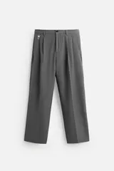 Pantalón gris de corte ancho con cintura elástica, pliegues frontales, bolsillos laterales y traseros de vivo. Incluye detalle de hebilla metálica en la trabilla y cierre frontal con cremallera y botón.