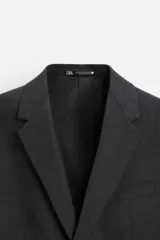 Blazer slim fit color gris oscuro confeccionado en tejido con viscosa. Tiene cuello con solapas de muesca, manga larga con puño abotonado, bolsillo de vivo en pecho, bolsillos de solapa en cadera, bolsillo interior, bajo con aberturas en espalda y cierre frontal con botones.
