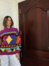 Sweater de lana merino color crema con cuello alto y diseño con motivos geométricos en amarillo, naranja, violeta y negro.