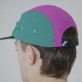 Gorra de cinco paneles con visera plana, color negro con secciones en verde y fucsia.