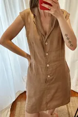 Vestido corto color marrón claro, con cuello camisero, sin mangas y abotonado al frente. Confeccionado en lino y algodón.