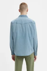 Camisa de denim celeste de corte recto, con mangas largas, cuello clásico, cierre con botones a presión, dos bolsillos con solapa abotonada en el pecho y canesú en la espalda.