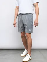 Bermuda de felpa gris con efecto lavado, confeccionada en mezcla de poliéster y algodón. Presenta un cordón ajustable en la cintura y el logo Umbro en la pierna izquierda.