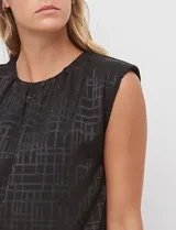 Blusa de gasa color beige con textura labrada, sin mangas, con hombreras internas y abertura en la espalda con botón.