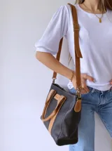Cartera negra de cuero con forro de tela, doble asa corta color camel y correa larga desmontable también color camel.