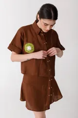 Camisa corta de manga corta color rojo, con doble cartera diagonal con botones de madera, cuello clásico y botamangas marcados. Tiene un bolsillo con aplique de crochet hecho a mano con forma de frutilla.