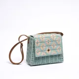 Bandolera celeste de paja trenzada con diseño geométrico en beige y correa de cuero sintético marrón.