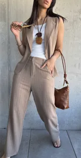 Conjunto sastrero tostado con rayas verticales finas, compuesto por un pantalón de corte recto y un chaleco sin mangas con solapas. El pantalón tiene cierre frontal con botón y bolsillos laterales. El chaleco tiene un botón frontal y bolsillos simulados.