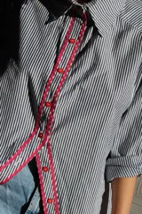 Camisa de poplin negro rayado con corte cómodo, mangas 3/4 y detalles ondeados al frente con zigzag de algodón fucsia y botones fucsia.